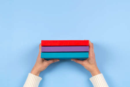 Female hands holding pile of books over light blue background. Education, self-learning, hobby, relax time at homeの写真素材