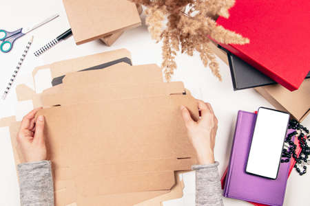 Top view to woman hands folding paper package box on the table. Startup small business freelance...