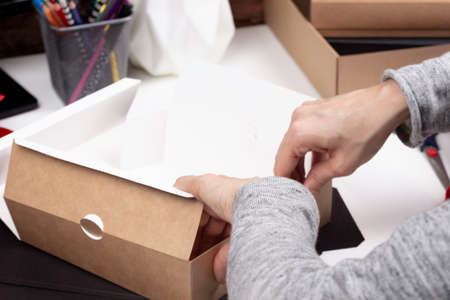 Woman hands folding paper package box on the table. Startup small business freelance workspace, online marketing, handmade craft, self employed, small family business conceptの写真素材