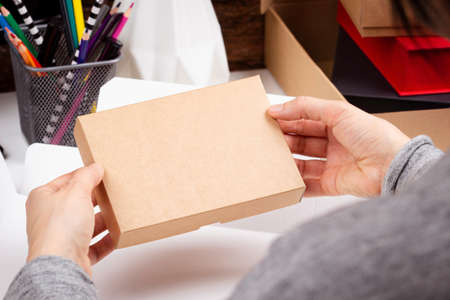 Female hands holding paper package box. Woman working in her workplace at home. Startup small...
