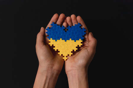 Child hands holding Ukraine flag colors heart on black background. Top view