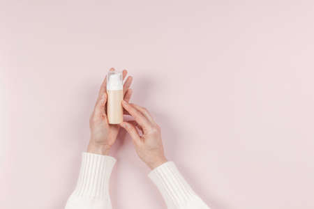 Woman hands holding cosmetic bottle for gel, face cream, CC, BB face cream toner, make up foundation on pastel pink background. Blank plastic package container mock up with place for textの写真素材