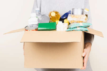 Woman hands holding cardbox with grocery products. Volunteer collecting food into donation box....