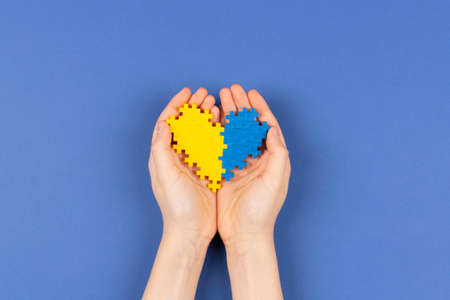 World Down syndrome day background. Hands holding blue and yellow Down syndrome awareness day heart on navy blue background. Top view, copy spaceの写真素材