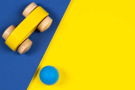 Abstract minimal kid toys background. Small yellow wooden car and blue toy ball on geometric yellow...