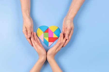 World autism awareness day concept. Adult and child hands holding puzzle heart on light blue background. Top viewの写真素材