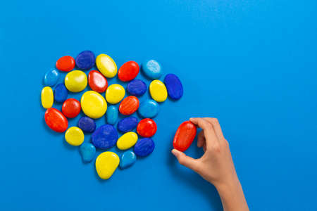 World autism awareness day. Kid hand make heart from colorful painted beach pebble stones over blue background. Top viewの写真素材