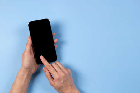 Female hand touching smartphone display and pointing with index finger on blank mobile phone screen...