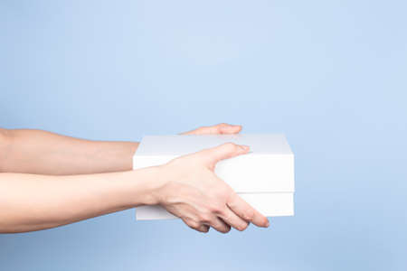 Woman hands holding white cardboard box on light blue background. Blank white color parcel box....