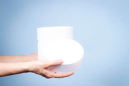 Woman hands holding white round cardboard box and open cap on light blue background. Mock up package...