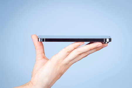Woman hand holding smartphone screen face up side view on light blue backgroundの写真素材