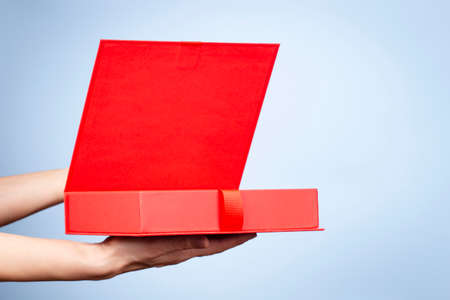 Female hands opening red elegant luxury box with ribbon. Mockup present gift box on light blue...