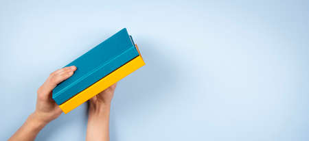 Female hands holding two blue and yellow color books over light blue background. Education, self-learning, book swapの写真素材