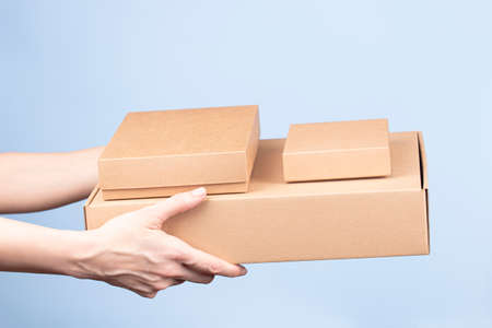 Stack of cardboard boxes in female hands. Blank brown parcel boxes on light blue background....