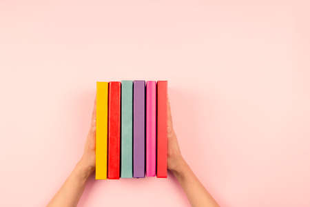 Female hands holding pile of books over pastel pink background. Education, self-learning, hobby, relax time at homeの写真素材