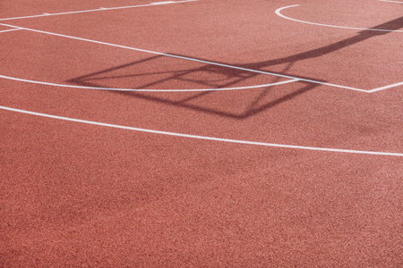 Shadow of the rack with shield and basketball ring on orange basketball rubber field ground during sunny day outdoors. Basketball game backgroundの写真素材