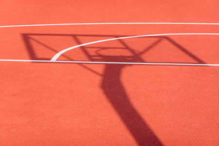 Shadow of the rack with shield and basketball ring on orange basketball rubber field ground during sunny day outdoors. Basketball game backgroundの写真素材