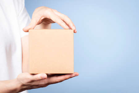 Female hands holding brown rectangular cardboard box on light blue background. Mockup parcel box. Packaging, shopping, delivery conceptの写真素材