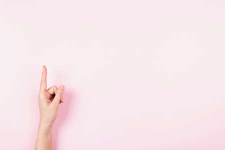 Woman hand pointing up with index finger to something virtual and invisible, copy space on pastel pink background. Hand gesture, number oneの写真素材