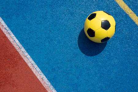 Colorful sports court background. Top view light blue and red field rubber ground with white line and yellow soccer ball on sunny day outdoorsの写真素材