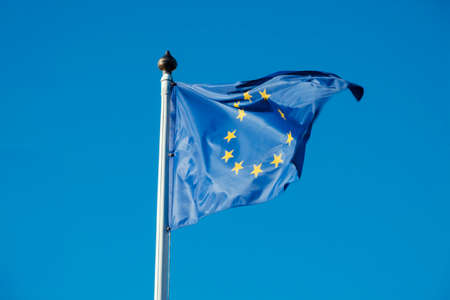 Flag of European Union waving in the wind on flagpole against blue sky on sunny dayの写真素材