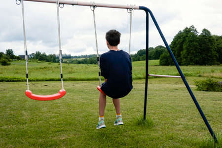 Sad lonely young teenage boy sitting on swings outdoorsの写真素材