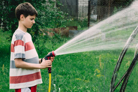 Child watering plants in garden. Kid with water hose gardening outdoor in countryside holidays village.の写真素材