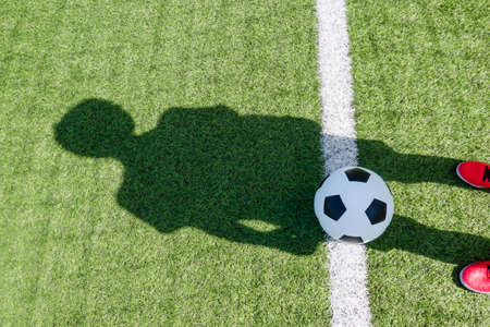 Soccer football sport background. Soccer ball and shadow of player on artificial turf soccer field in sunny day outdoorsの写真素材
