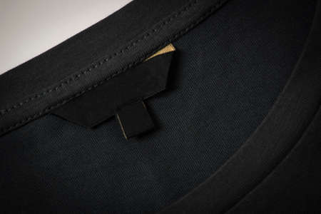 Black blank clothes label on black fabric texture background. Top view
