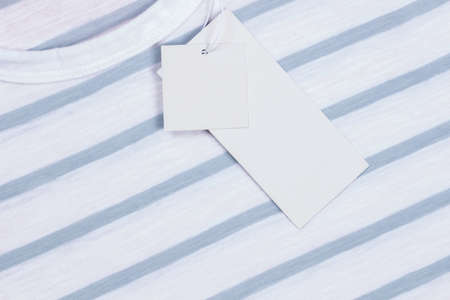 Blank white rectangular label tags on striped t-shirt clothes background. Price tag tabel mock up with copy spaceの写真素材