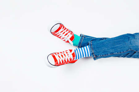 Kid wearing different pair of socks. Child foots in mismatched socks and red sneakers sitting on...
