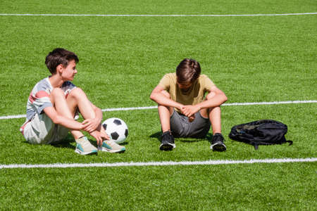 Children talking in school stadium outdoors. Teenage boy comforting consoling upset sad friend. Education, bullying, conflict, social relations, problems at school, learning difficulties conceptの写真素材