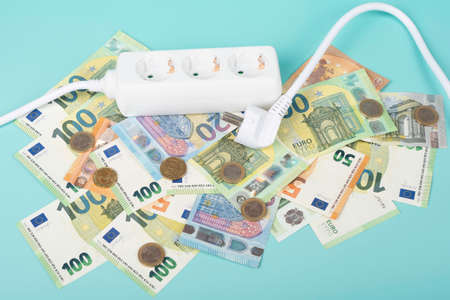 Electric power strip extension cord and Euro money banknotes on light blue background. Rising...