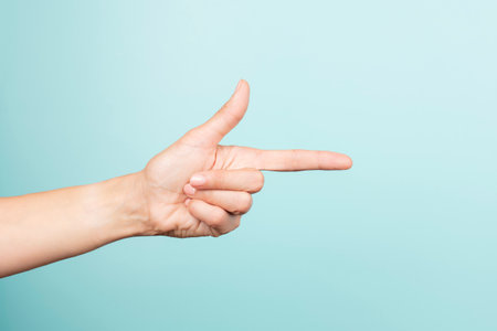 Woman hand pointing gesture. Female hand points finger at something on light blue background. Front...