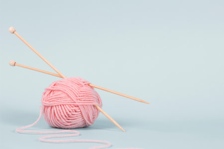 One thread ball and wooden bamboo knitting needles on light blue background. Hobby, relaxation,...