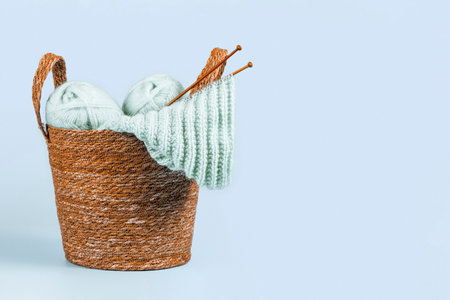 Knitting background. Knitting yarn, bamboo needles and new started knitted sweater in basket on light blue background. Handmade hobby, relaxation at home, mental health, sustainable lifestyleの写真素材