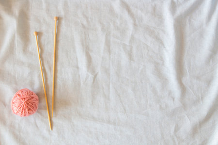 Pink thread ball with wooden bamboo knitting needles on white linen fabric background. Top view, copy space. Hobby, relaxation, mental health, sustainable lifestyleの写真素材