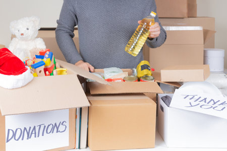 Christmas donations for charity. Man volunteer collecting food, clothes, kid toys, books into...