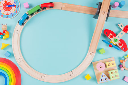 Baby kids toys frame background. Wooden railway with train and collorful sustainable educational toys on light blue background. Montessori, eco-friendly toys for children. Top view, flat layの写真素材