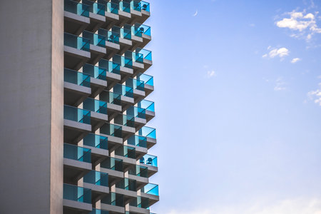 Fragment of white modern residential apartment house, hotel building with glass balconies on blue...