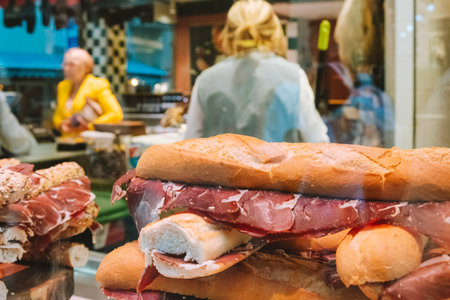 Typical Spanish sandwich with ham meat Jamon in showcase of local shop with unrecognizable people in backgroundの写真素材