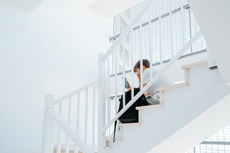 Sad teenage boy with mobile phone and backpack sitting on stairs. Teenager surfing on Internet, watching video, using app. Education, learning difficulties, mobile addiction conceptの写真素材