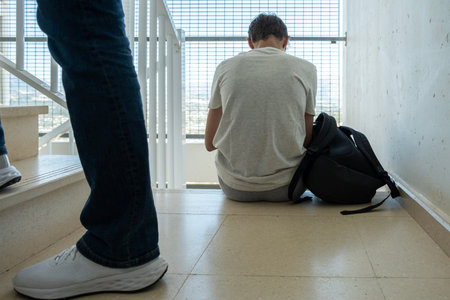 Sad teenage boy with mobile phone and backpack sitting on stairs. Teenager surfing on Internet, watching video, using app. Education, learning difficulties, mobile addiction conceptの写真素材