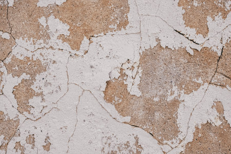 Old cracked weathered painted wall background texture. Beige dirty peeled plaster wall with falling...