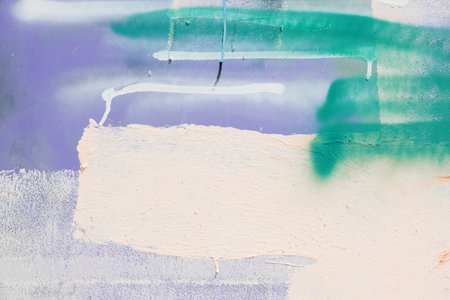 Messy paint strokes and smudges on painted stucco wall background. Abstract wall surface with part of graffiti. Purple, white, beige, green color drips, flows, streaks of paint and paint spraysの写真素材