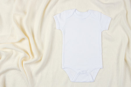 Top view to white cotton baby short sleeve bodysuit on beige blanket throw background. Blank gender neutral newborn bodysuit mock up templateの写真素材