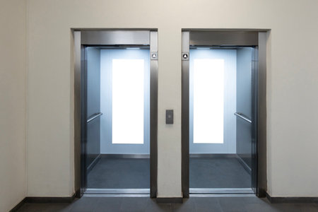Mock up. Two empty elevators with opened metallic cabins doors and vertical poster media template frames hanging on cabin wall insideの写真素材
