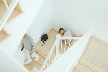 Sad frustrated teenage boy with backpack sitting on staircase while his friend walks away. Education difficulties, problem with friends, family, emotion in adolescence conceptの写真素材