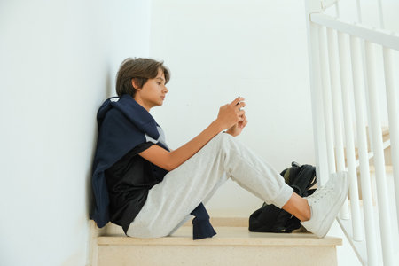 Teenage boy sitting on stairs and using smartphone. Teenager browse social media, communicate with friends, family, play games, watch videos, use apps for entertainmentの写真素材