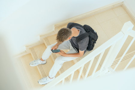 Teenage boy sitting on stairs and using smartphone. Teenager browse social media, communicate with friends, family, play games, watch videos, use apps for entertainmentの写真素材